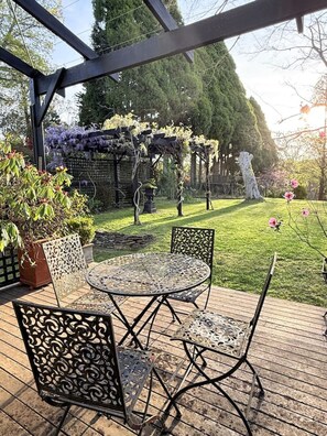 Ein überdachter Patio-Bereich mit einem runden Metalltisch und Stühlen, umgeben von einer Holzterrasse.