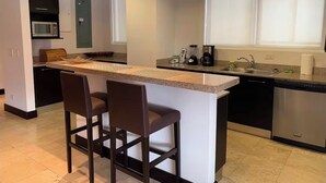 Una cocina moderna con una isla central, taburetes de bar, microondas, cafetera y lavavajillas.