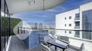 A modern balcony with a glass table and wicker chairs, a blue mosaic wall, and a view of a white building. - Bloomfields Classic 2Br With Private (Dubai)