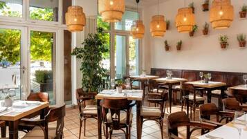 A restaurant with wooden tables and chairs, hanging wicker lamps, and potted plants on the walls.