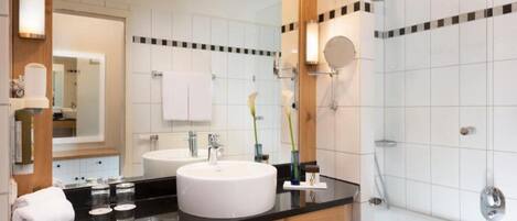 A modern bathroom with a large mirror, two sinks, a bathtub, and a vanity with a black countertop.