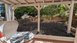 A covered patio area with a table and chair, surrounded by a stone wall and trees. - Apartment Oasis Costa Calma (Costa Calma)