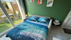 A bedroom with a large bed, a view of the garden through a sliding door, and a small table with a lamp. - Studio apartment on the first floor with outdoor area and parking space (Merlimont)