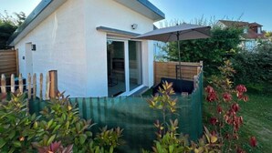 A small, single-story house with a sloped roof, a sliding glass door, and a patio area with a table and chairs. - Studio apartment on the first floor with outdoor area and parking space (Merlimont)