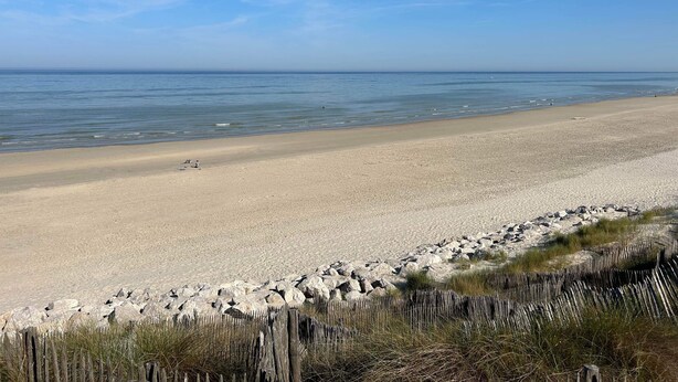 A beach with a wooden fence and rocks in the foreground, a sandy beach, and calm water. - Studio apartment on the first floor with outdoor area and parking space (Merlimont)