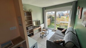 A living room with a sofa, TV, and a sliding glass door leading to a backyard. - Studio apartment on the first floor with outdoor area and parking space (Merlimont)