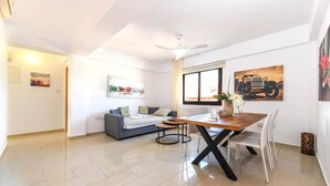 A modern living room with a dining area, featuring a sofa, a table, and artwork on the walls. - Nissi Apartment 101 (Ayia Napa)