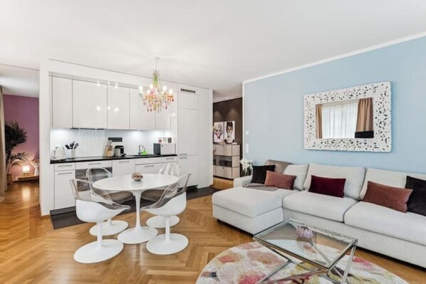 A modern living room with a white sofa, a glass coffee table, and a dining area with a white table and chairs. - Central | Prime Location | Air Conditioning | Free Parking (Zürich)