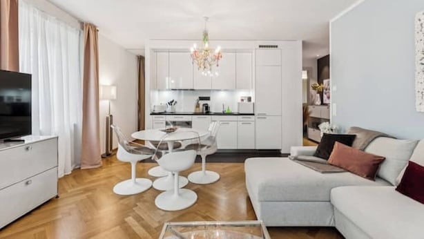 En moderne stue med sofa, sofabord og spiseområde med lysekrone.