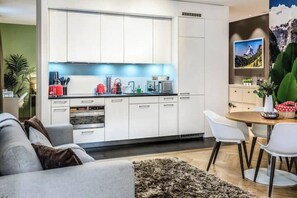 A modern kitchen with white cabinets, a dining area with a round table and white chairs, and a living room with a grey sofa. - Boutique | CentralLocation | AC | SwissExperience (Zürich)