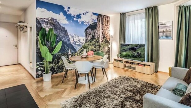 Een moderne woonkamer met een bergdecoratie, een eethoek met een ronde tafel en stoelen, een flatscreen televisie en een gezellige bank.
