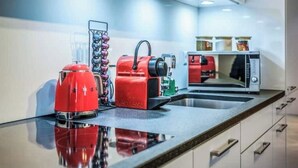 Een moderne keuken met een roestvrijstalen aanrecht, een rode koffiezetapparaat, een rode elektrische waterkoker, een groene elektrische waterkoker en een magnetron.