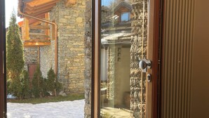 A room with a sliding glass door leading to an outdoor area with a stone wall and wooden beams. - Brenlo (La Salle)