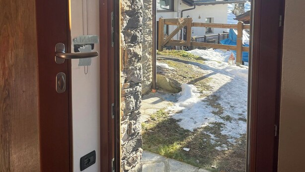 A wooden door leading to a stone wall with a view of a snow-covered yard and a building with a wooden fence. - Brenlo (La Salle)