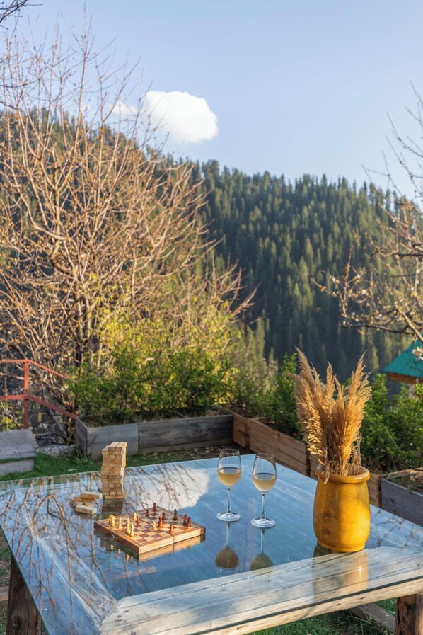 A glass-top table with a chessboard, two wine glasses, and a vase of pampas grass. - ELIVAAS Skylounge 4 BHK with Garden  (Kumharsain)