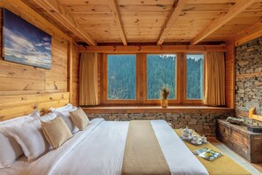 A wooden cabin room with a bed, a stone fireplace, and a window with curtains. - ELIVAAS Skylounge 4 BHK with Garden  (Kumharsain)