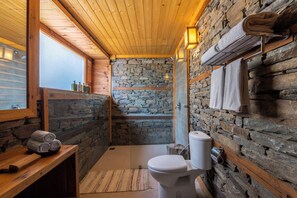 A bathroom with stone walls, wooden ceiling, a toilet, a sink, and a towel rack. - ELIVAAS Skylounge 4 BHK with Garden  (Kumharsain)