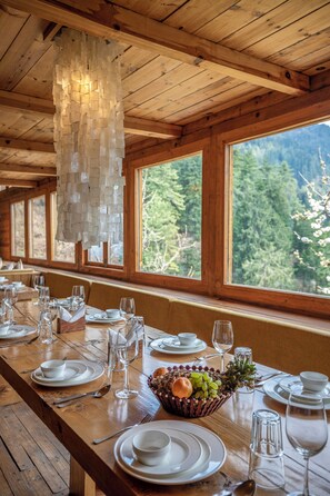 A wooden dining table set with white plates, glasses, and a fruit basket. - ELIVAAS Skylounge 4 BHK with Garden  (Kumharsain)