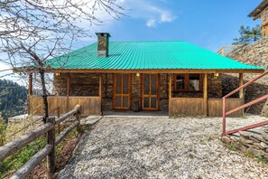 A stone building with a green roof and wooden exterior, featuring a stone staircase and a gravel pathway. - ELIVAAS Skylounge 4 BHK with Garden  (Kumharsain)