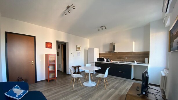Eine moderne Wohnung mit Wohnzimmer, Essbereich und Küche. Sie verfügt über Holzboden, weiße Wände und eine braune Tür.