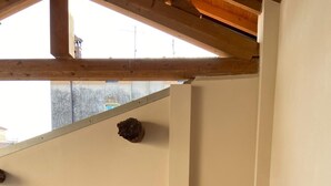Ein Blick in den Raum zeigt drei terrakottafarbene Sessel und einen kleinen Tisch, eine Betonwand und einen Holzbalken an der Decke.