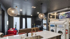 Ett modernt hotellrum med ett litet kök, ett matbord och en våningssäng samt tvättmaskiner.