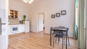 Ett modernt kök med vita skåp och en inbyggd ugn, en matplats med bord och stolar samt en hall som leder till ett annat rum.
