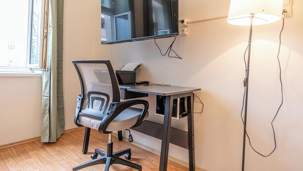 Ett rum med ett skrivbord, en stol, en tv, en lampa och ett fönster med gardiner.