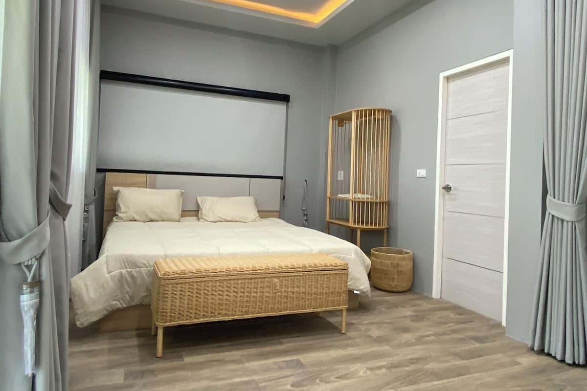 A modern bedroom with a bed, a bedside table, a wicker bench, a wooden cabinet, and a door.