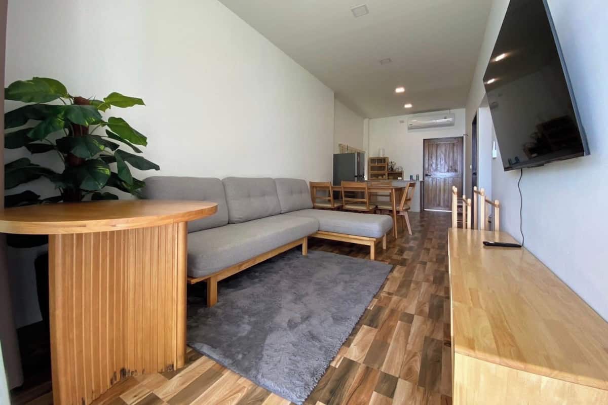 A modern living room with a grey sofa, wooden coffee table, and a large plant.