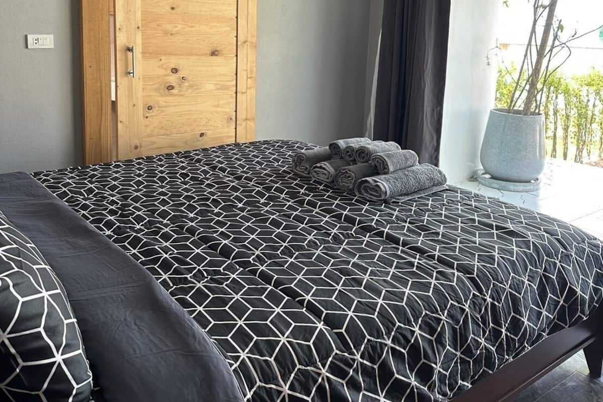 A bedroom with a bed, a wooden wardrobe, an air conditioning unit, and a view of greenery outside.
