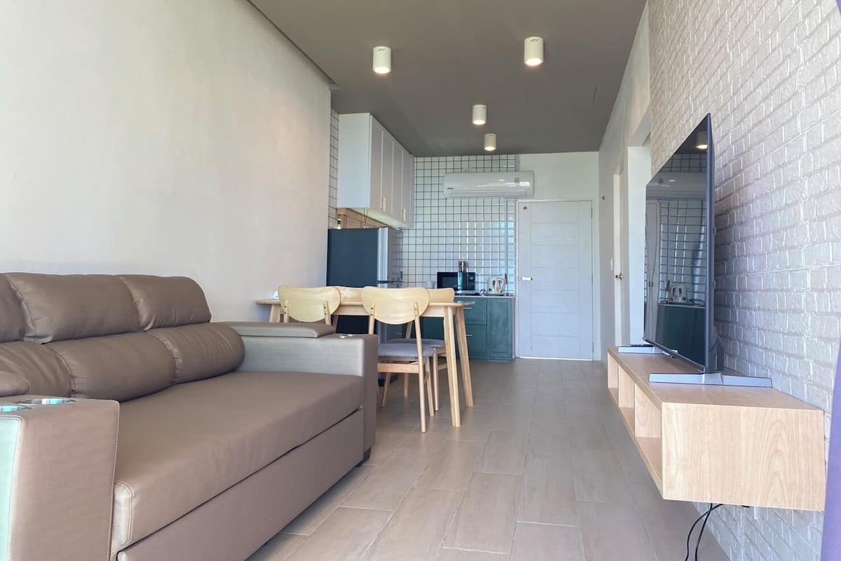 A modern living room with a sofa, a dining table with chairs, and a kitchen area with a microwave and cabinets.