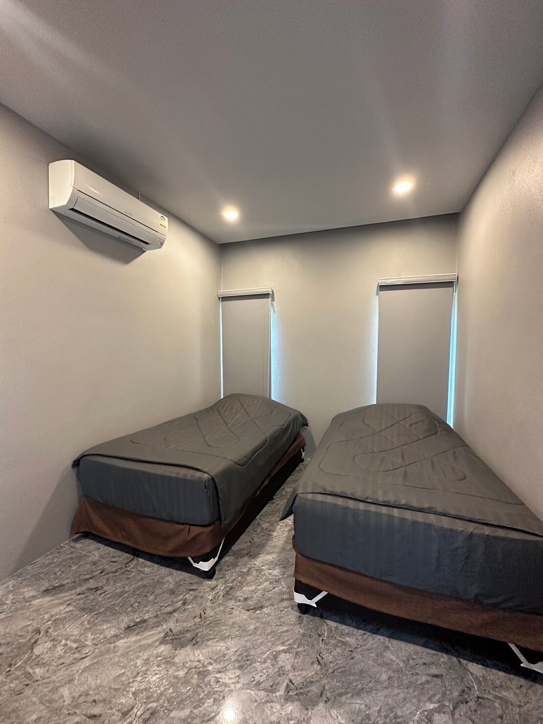 Una habitación pequeña con dos camas individuales, aire acondicionado instalado en la pared y piso de mármol.