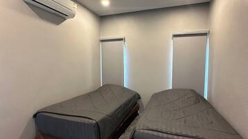 Una habitación pequeña con dos camas individuales, aire acondicionado instalado en la pared y piso de mármol.