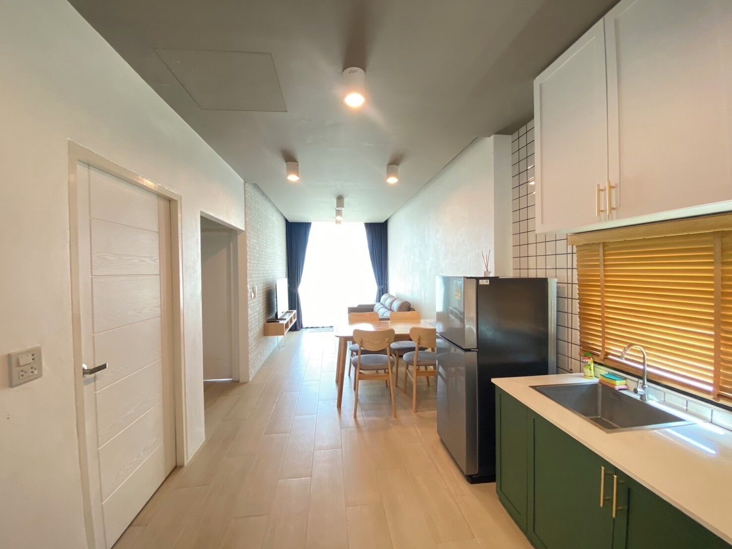 Une cuisine moderne dotée d’un réfrigérateur encastré, un coin repas avec une table et des chaises, et un couloir menant à une chambre.
