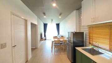 Une cuisine moderne dotée d’un réfrigérateur encastré, un coin repas avec une table et des chaises, et un couloir menant à une chambre.