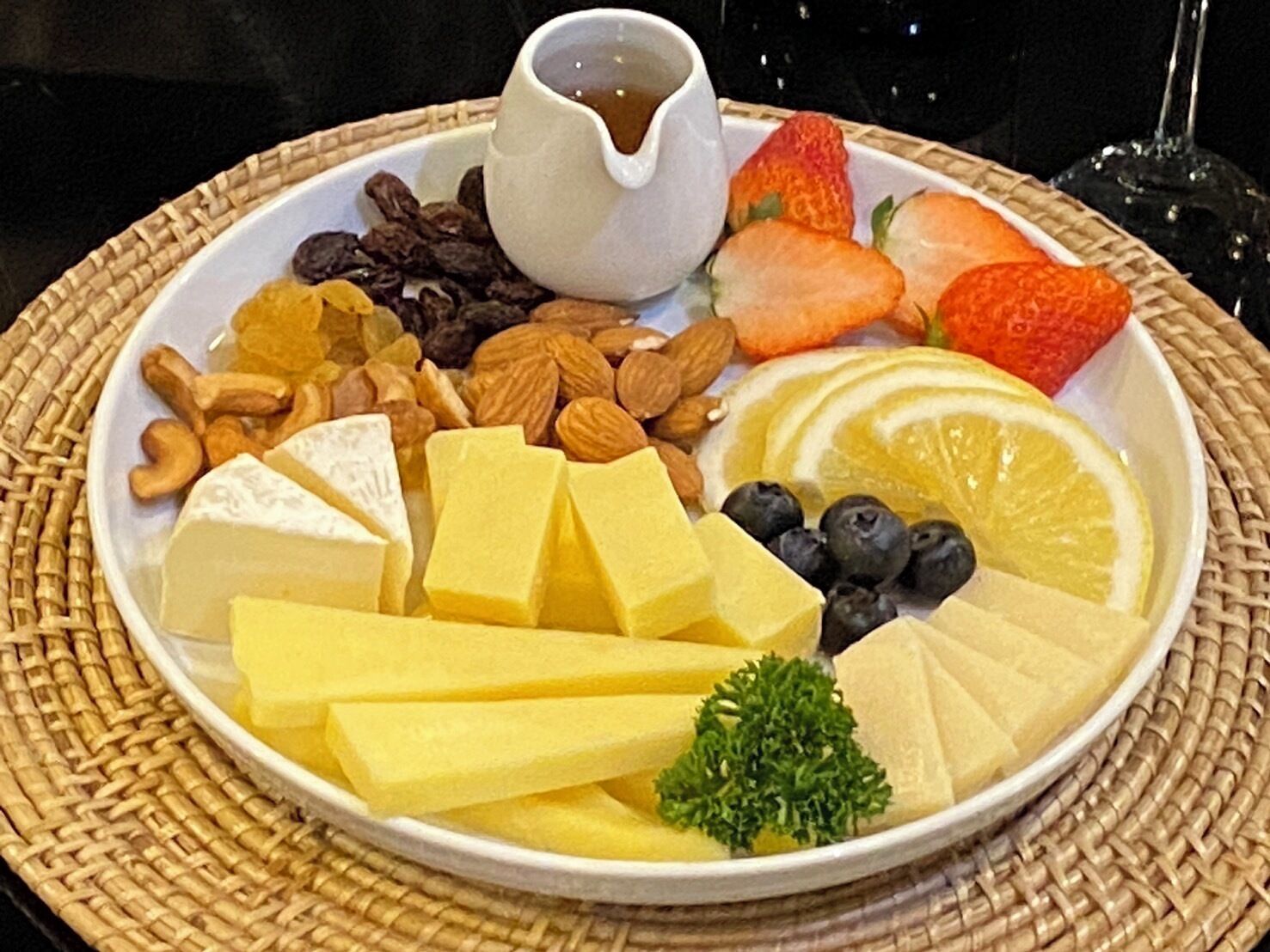 Un plato con varios quesos, frutas, frutos secos y un recipiente pequeño con salsa.