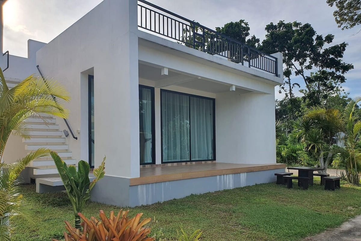 A modern two-story house with a balcony, large windows, and a well-maintained lawn.