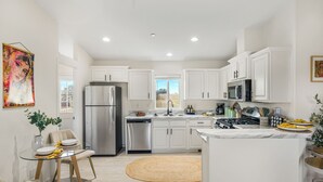 Una cocina moderna con armarios blancos, electrodomésticos de acero inoxidable y un comedor con mesa y sillas de vidrio.