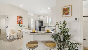 Una cocina moderna con armarios blancos, una isla de mármol y una zona de comedor con dos taburetes.