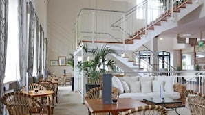 A spacious lobby with high ceilings, a central seating area with a sofa and chairs, a staircase, and a large window providing natural light. - Sunday Resort Rugen Superior Double Room (Sagard)
