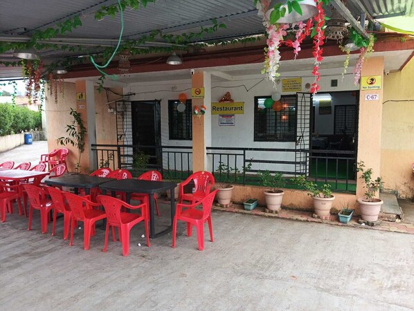 Un restaurante al aire libre con sillas y mesas de plástico rojo, plantas en macetas y un cartel que indica que es un restaurante.