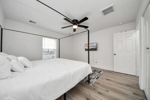 A bedroom with a bed, a ceiling fan, a window, a door, and a painting on the wall. - The Ivory House- Gated 2BR Urban Escape- Downtown HTX- Medical Center (Houston)