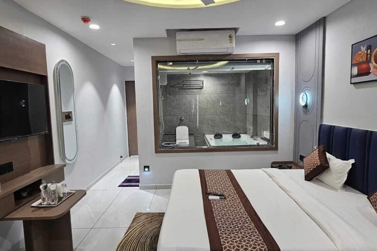 Une chambre d’hôtel moderne équipée d’un grand lit, d’une télévision, d’un miroir, d’une douche et d’un climatiseur fixé au mur.