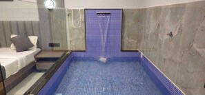 Un bagno moderno con doccia vetrata, vasca da bagno con piastrelle blu e un letto con cuscino grigio.