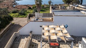 Een terras op het dak met uitzicht op een wateroppervlak, een palmboom en een zonnepaneel.