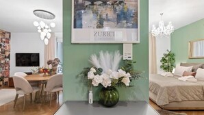 A modern living room with a dining area, a mounted picture of Zurich, a vase with flowers, and a chandelier. - Central | AC | Private Terrace | Free Parking (Zürich)