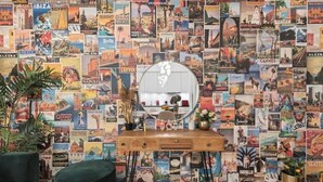 A room with a wall covered in travel posters, a round mirror, a wooden desk, and a green chair. - Central | AC | Private Terrace | Free Parking (Zürich)
