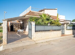 Ein Wohnhaus mit befahrbarer Einfahrt, überdachter Terrasse und kleiner Sitzgelegenheit im Freien.
