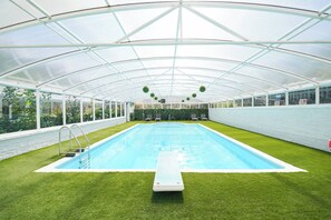 A covered swimming pool with artificial grass, a diving board, and a greenhouse structure.